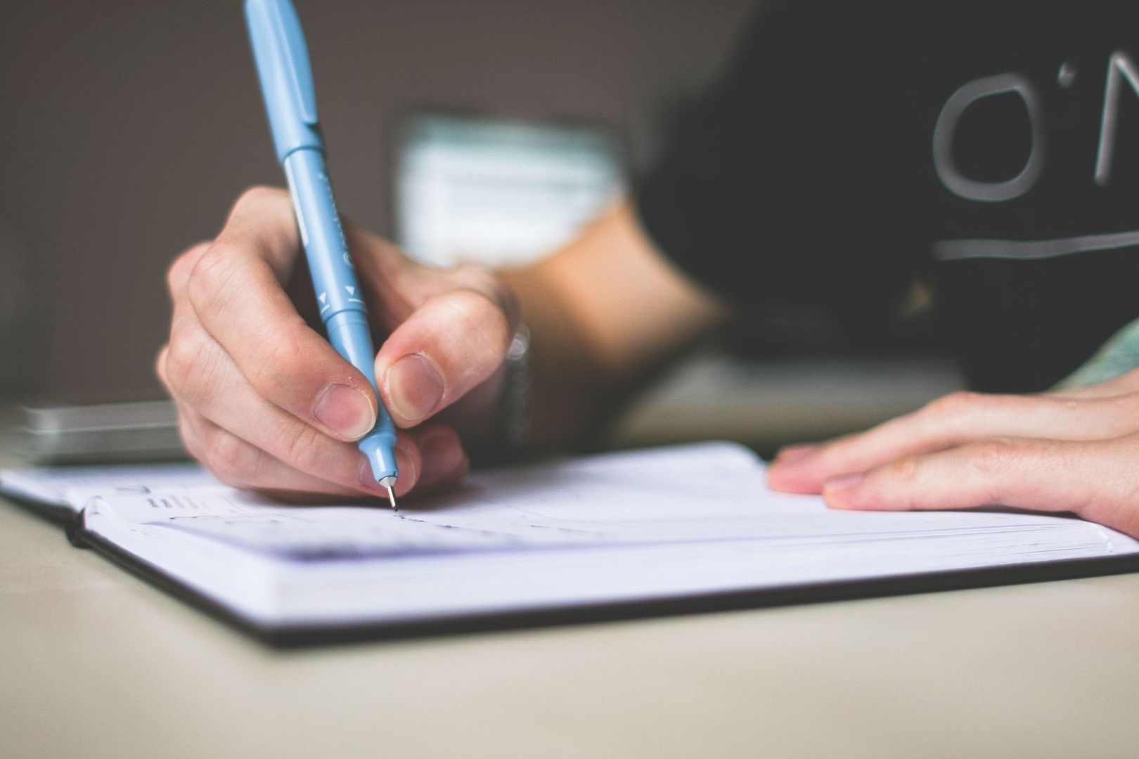 Close-up of a person writing in a notebook with a blue pen