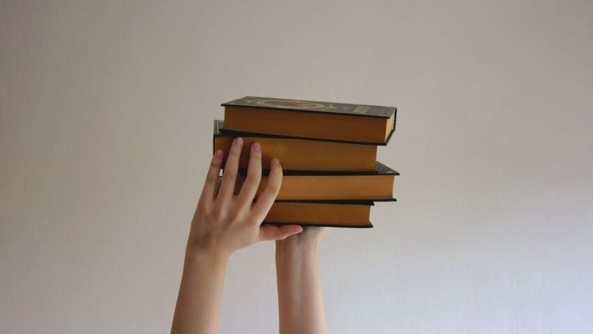 Hands hold a stack of vintage books against a plain wall