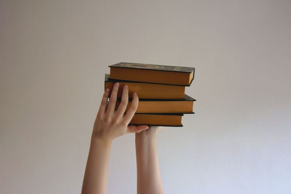 Hands hold a stack of vintage books against a plain wall